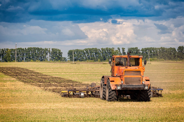 Un tractor moderno naranja arada la tierra i
 - Foto, imagen