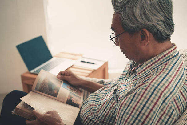 Senior man is het lezen van een boek in woonkamer. - Foto, afbeelding
