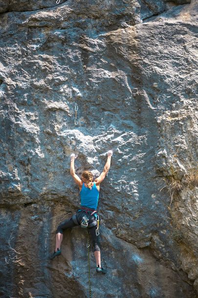 Альпініст тренується підніматися на скелю. Сильна дівчина долає важкий скелелазний маршрут. Активний спосіб життя. Екстремальне хобі. Жінка займається спортом на природі
. - Фото, зображення