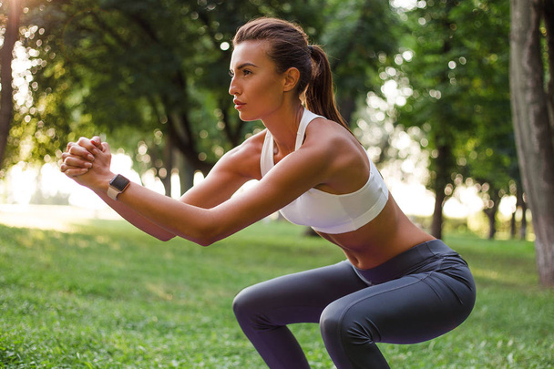 Beautiful squat. Young beautiful fit woman in sportswear exercising in green park - Zdjęcie, obraz