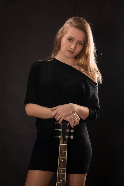 Beautiful girl with guitar on black background. - Фото, изображение