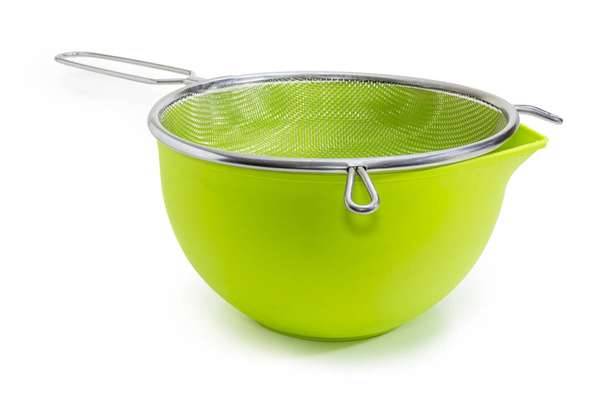 Green bowl and round stainless steel sieve with wire mesh at selective focus on a white background - Photo, Image