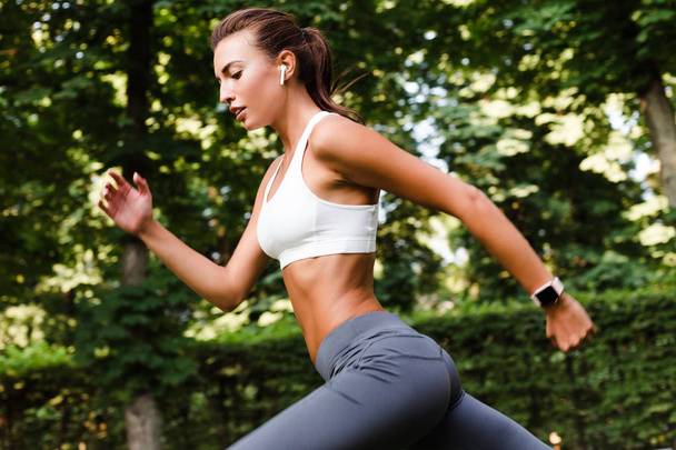 Intenso entrenamiento. Vista lateral de la joven mujer en forma hermosa en ropa deportiva ejercicio en el parque verde
 - Foto, imagen