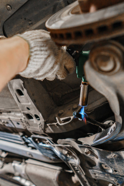 Mécanicien de voiture inspectant la roue de la voiture et réparer les détails de suspension. Voiture relevée à la station-service de réparation. remplacement de la virole et du levier - Photo, image