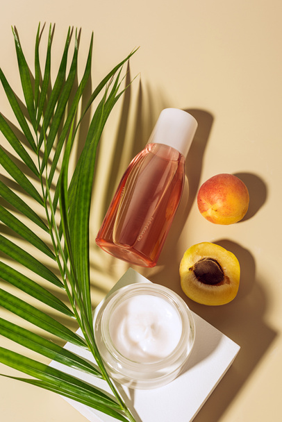 flat lay with body cream and lotion, apricots and green palm leaf on beige background - Fotografie, Obrázek