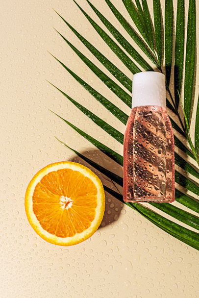 vista superior da folha de palma, água micelar para cuidados com a pele em garrafa e laranja metade no fundo bege
 - Foto, Imagem