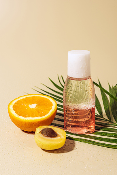 Vista de cerca del agua micelar para el cuidado de la piel en botella y mitad naranja sobre fondo beige
 - Foto, imagen
