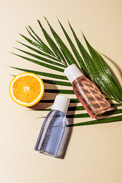 flat lay with micellar water in bottles, green palm leaf and orange half with water drops on beige backdrop - Fotoğraf, Görsel