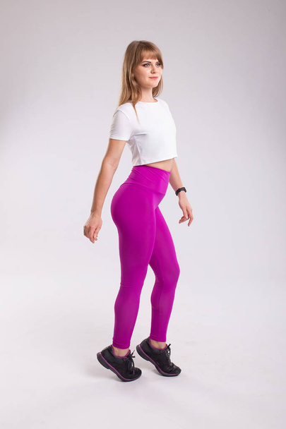Side profile view portrait of beautiful happy cheerful healthy sporty woman wearing pink leggings and white top. Isolated on white background - 写真・画像
