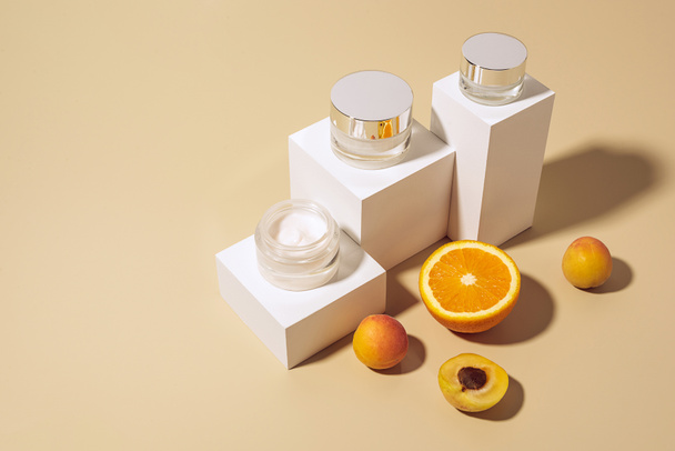 Vista de cerca de las cremas y frutas dispuestas para el cuidado de la piel sobre fondo beige
 - Foto, Imagen