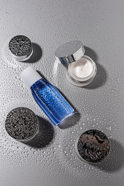 top view of micellar water and body creams with water drops on grey background - Photo, Image