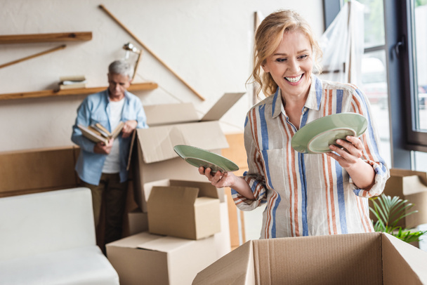 smiling woman packing plates and husband standing behind during relocation  - Photo, Image