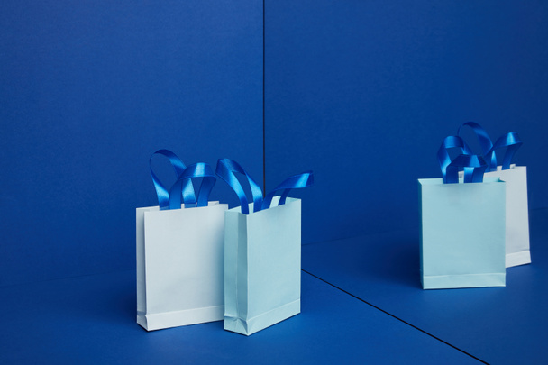 close up view of arranged paper shopping bags with mirror reflection on blue background - Fotoğraf, Görsel
