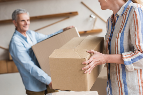 обрезанный снимок пожилой пары, держащей картонные коробки во время переезда
 - Фото, изображение