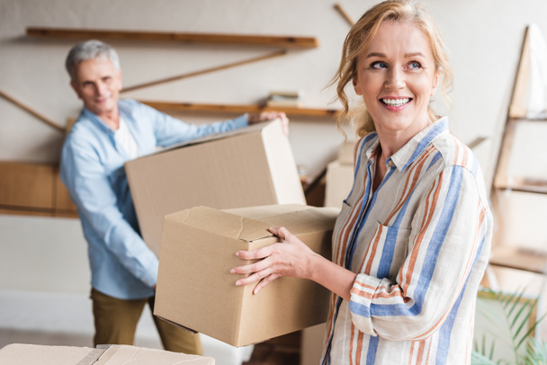 happy elderly couple holding cardboard boxes while moving home  - Photo, Image