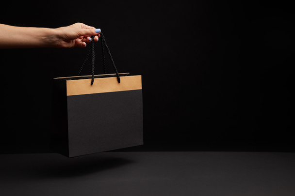 partial view of woman holding black shopping bag on black backdrop - Photo, Image