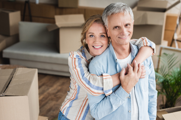 Gelukkig bejaarde echtpaar knuffelen en glimlachend in de camera terwijl het bewegen van home - Foto, afbeelding