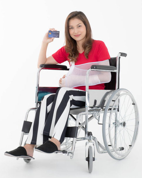Aziatische vrouw gebroken met arm sling gesponsord in haar handen zittend op een rolstoel ideeën voor ongeval letsel en gezondheidszorg Studio opname op een witte achtergrond. - Foto, afbeelding
