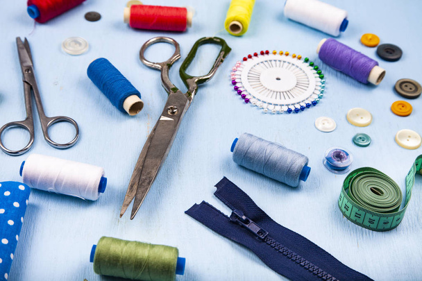 Sewing accessories on a blue wooden background. Measuring tape, pins, buttons, zipper, scissors and thread. - Photo, Image