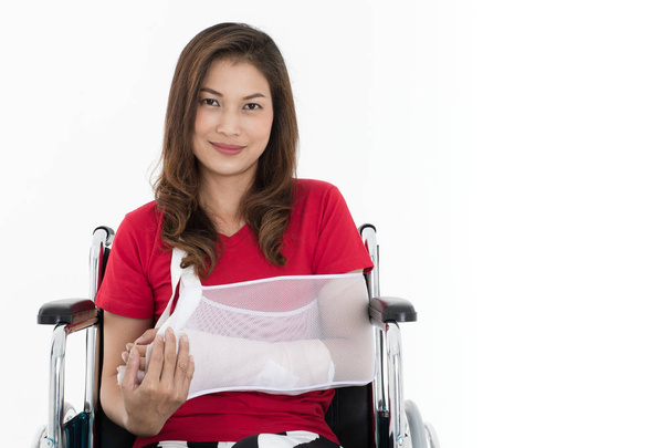Kırık kollu Asyalı kadın, elinde kol askısının sponsorluğunda tekerlekli sandalye üzerinde oturuyor. Beyaz bir arka planda yaralanmalar ve sağlık hizmetleri stüdyosu görüntüleri.. - Fotoğraf, Görsel