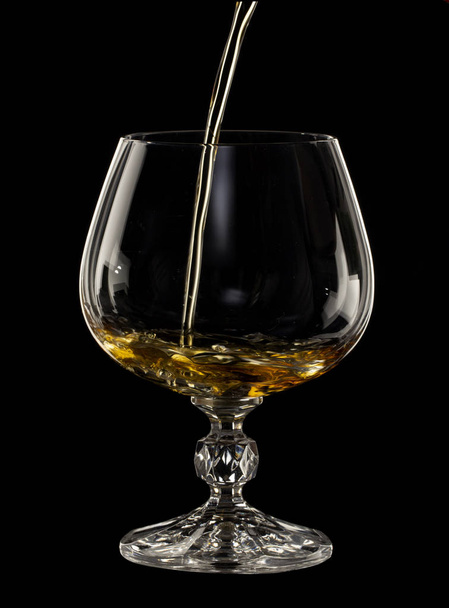 Cognac se vierte en un vaso, un spray de una bebida, sobre un fondo negro de cerca
 - Foto, imagen