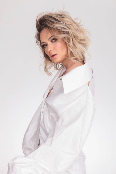 side view of sensual blonde woman wearing a bouffant white shirt while standing on white background - Foto, immagini
