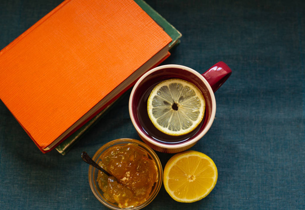Black Tea with Lemon, Half a Lemon, Books and Lemon Jam  on a Textile  Background. Autumn Concept - 写真・画像
