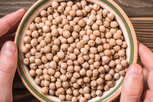 partial view of man holding bowl with raw chickpeas on wooden background - Photo, Image
