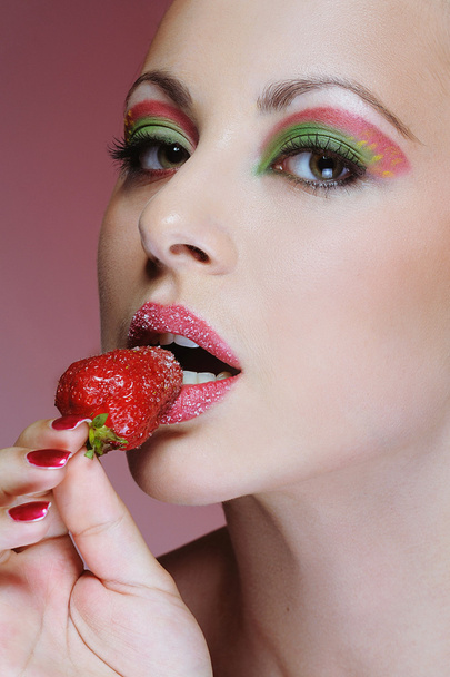 Close up young girl with bright makeup eating strawberry - Foto, afbeelding