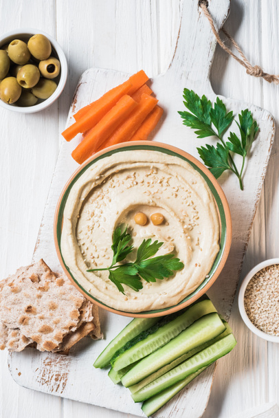 top view of hummus with parsley, cut vegetables and pita bread on wooden tabletop - Фото, изображение