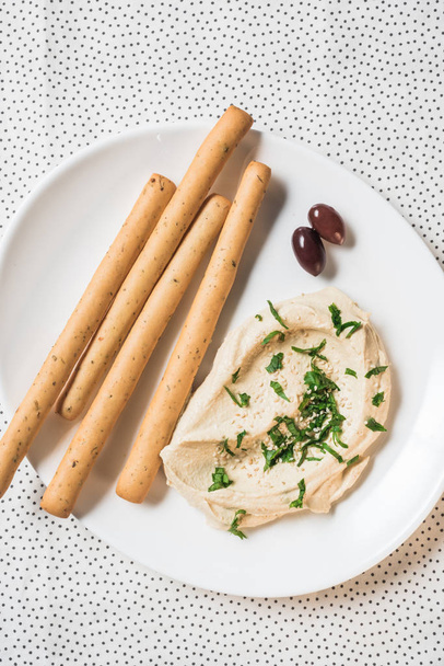 top view of hummus, breadsticks and olives on plate on linen - Foto, afbeelding