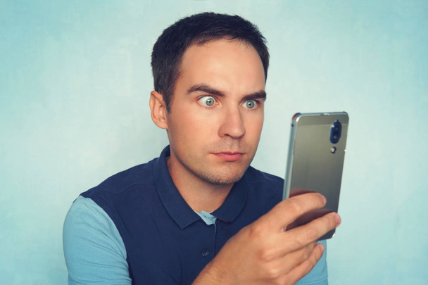 Um jovem espantado lê uma mensagem ao telefone. Chocado e surpreso asiático homem procurando smartphone
. - Foto, Imagem