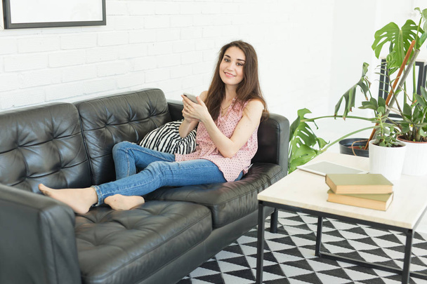 Pessoas, tecnologia e conceito de comunicação - Jovem mulher segurando smartphone enquanto se senta no sofá em casa
 - Foto, Imagem