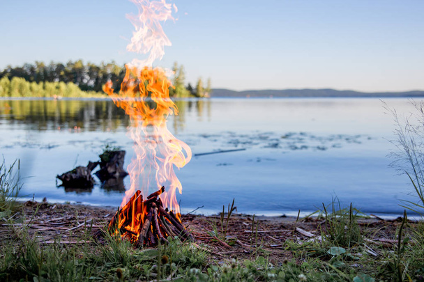 Beautiful campfire in the evening at lake. Fire burning in dusk at campsite - Photo, Image