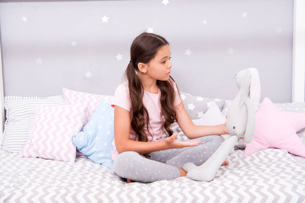 Child play grey rabbit. Best friends. Girl sit bed with grey bunny toy her bedroom. Kid prepare to go to bed. Wish sweet dreams to favorite toy. Girl kid relax and talk to bunny before fall asleep - Photo, image