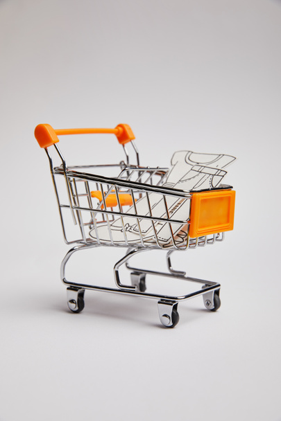 close up view of shopping cart with little clothes made of paper on grey background - Фото, изображение