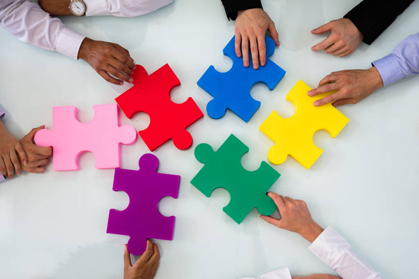 Group Of Businesspeople Colorful Solving Jigsaw Puzzle On Desk In Office - Fotografie, Obrázek