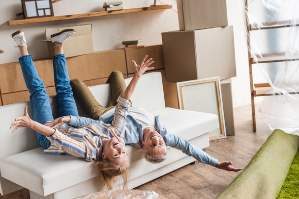 Aufgeregtes älteres Ehepaar liegt beim Umzug im neuen Haus auf Couch - Foto, Bild