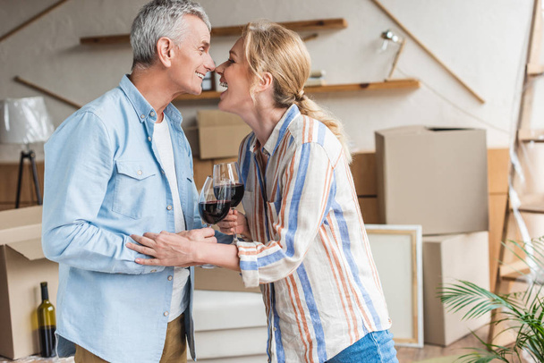 side view of happy senior couple drinking wine during relocation in new house - Photo, image
