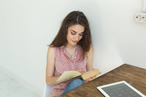 Lettura, educazione, cultura, concetto di persone: una giovane studentessa legge un libro, mentre è seduta su una sedia bianca in una stanza bianca
 - Foto, immagini
