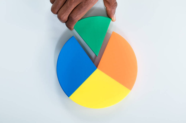 Overhead View Of Human Hand Taking Green Piece Of Pie Chart On Gray Background - Foto, immagini
