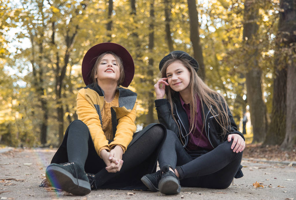 美しい少女が路上休憩します。感情的な会話姉妹。十代の少女は、残りの部分し、秋の公園で散歩の話。自然で若い学生をコミュニケーションします。. - 写真・画像