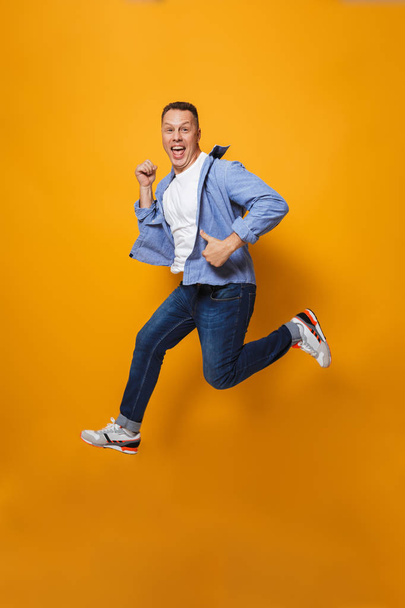 Image of emotional happy man jumping isolated over yellow background make thumbs up gesture. - Foto, afbeelding