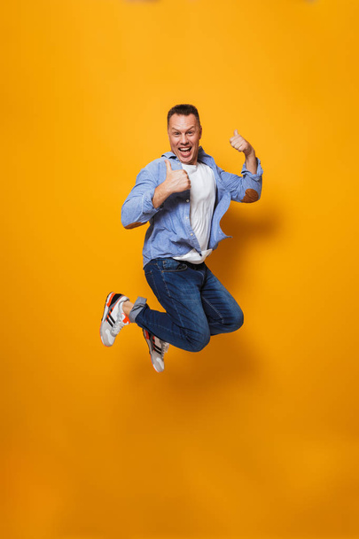 Image of emotional happy man jumping isolated over yellow background make thumbs up gesture. - Foto, Imagem