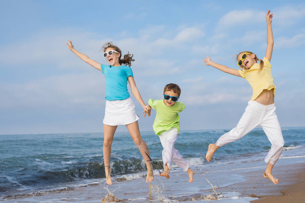Três crianças felizes a correr na praia durante o dia. Pessoas a divertir-se ao ar livre. Conceito de família amigável e de férias de verão
. - Foto, Imagem