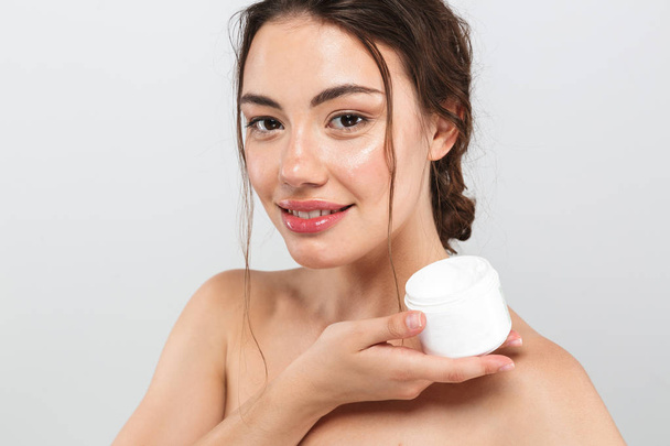 Beauty portrait of a lovely young topless woman with make-up holding container with body cream isolated over gray background - Φωτογραφία, εικόνα