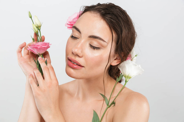 Beauty portrait of a lovely young topless woman with make-up posing with eustoma flowers at her face isolated over gray background - 写真・画像