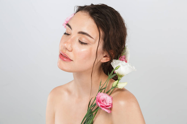 Beauty portrait of a beautiful young topless woman with make-up posing with eustoma flowers at her face isolated over gray background - Photo, image