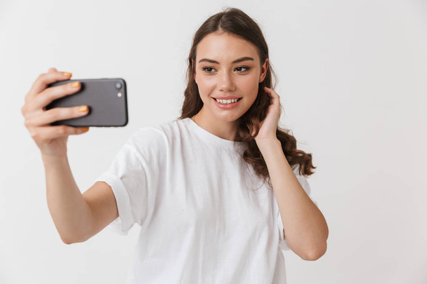 Retrato de una joven morena casual sonriente tomando selfie aislada sobre fondo blanco
 - Foto, Imagen