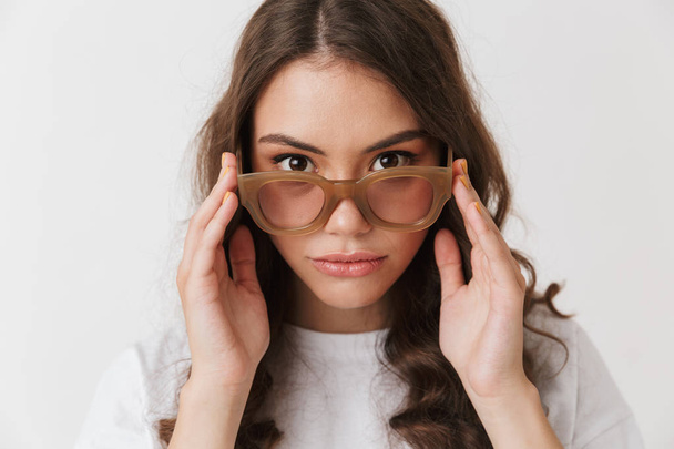 Portrait of an attractive young casual brunette woman in sunglasses looking at camera isolated over white background - Photo, image